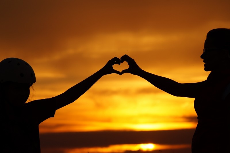 silhouette-of-mother-and-daughter-in-heart-shape-gesture-at-sunset